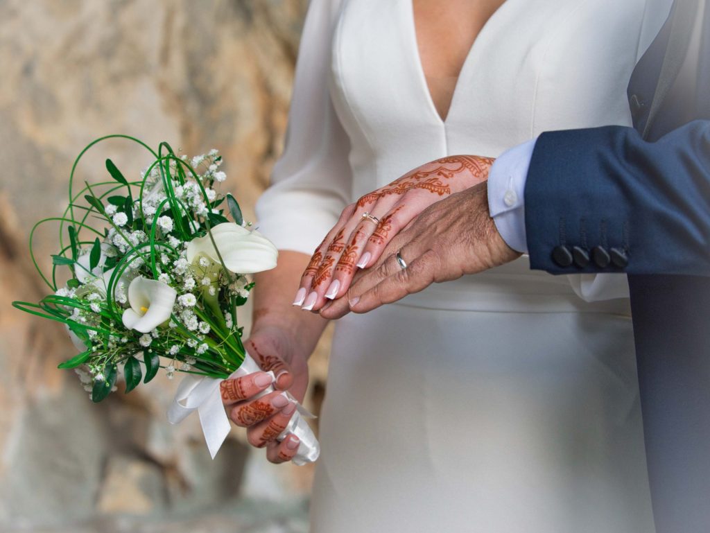 les mariés ont leurs mains l'une sur l'autre et la mariée tient un bouquet de fleurs