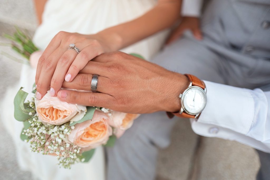 Mains des mariés avec leurs alliances, posées délicatement sur un bouquet de fleurs.
