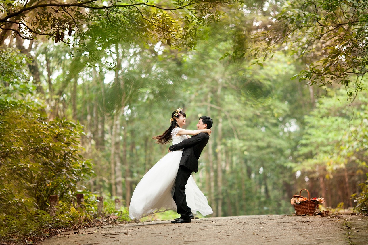 Le marié portant la mariée dans ses bras, tous deux souriant avec bonheur. Ils sont dans un parc ou une foret.