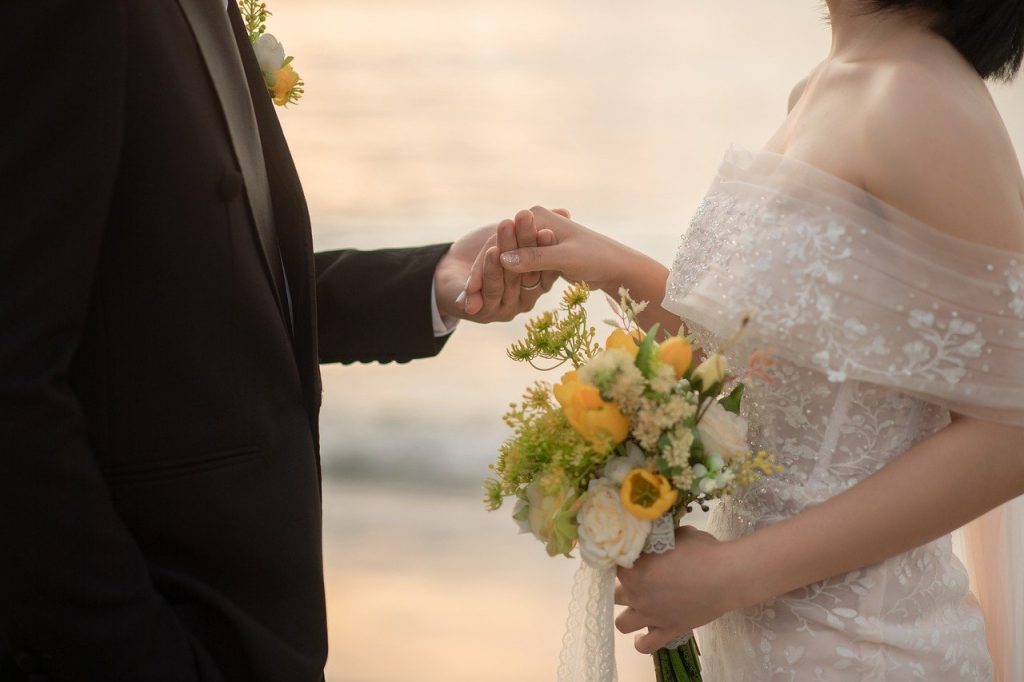 La mariée tenant la main du marié, tandis que ce dernier porte un bouquet de fleurs.