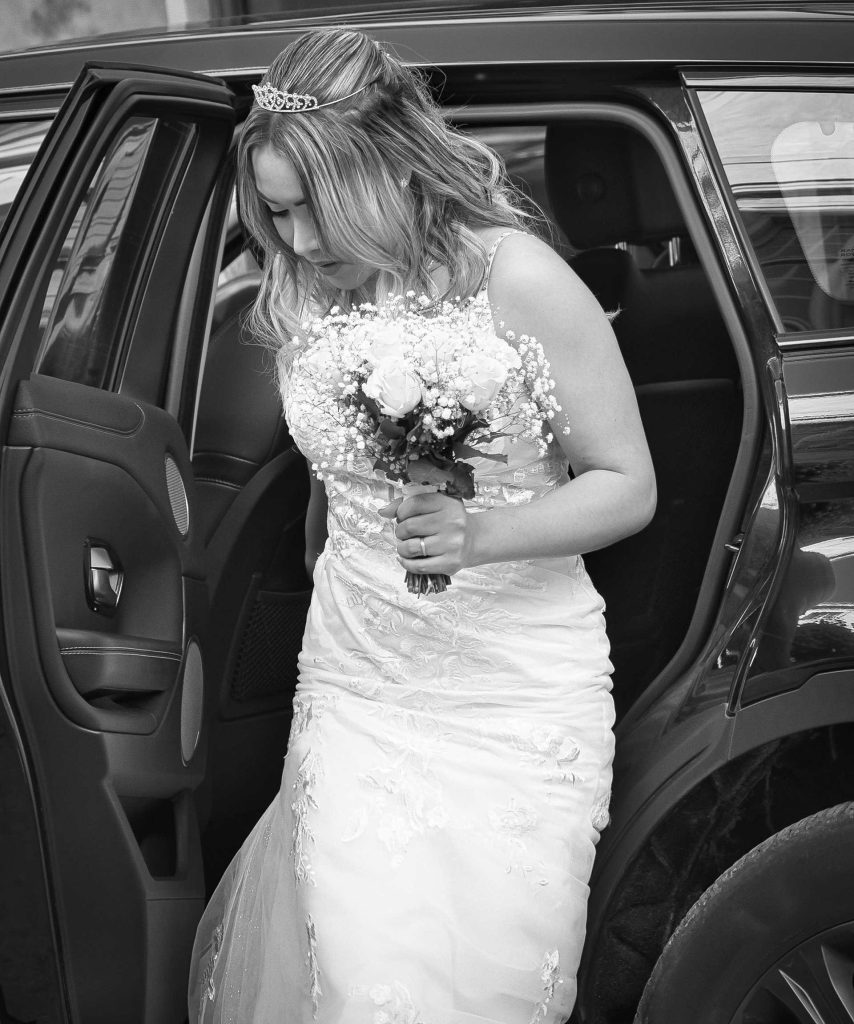 La mariée descend de la voiture un bouquet à la main