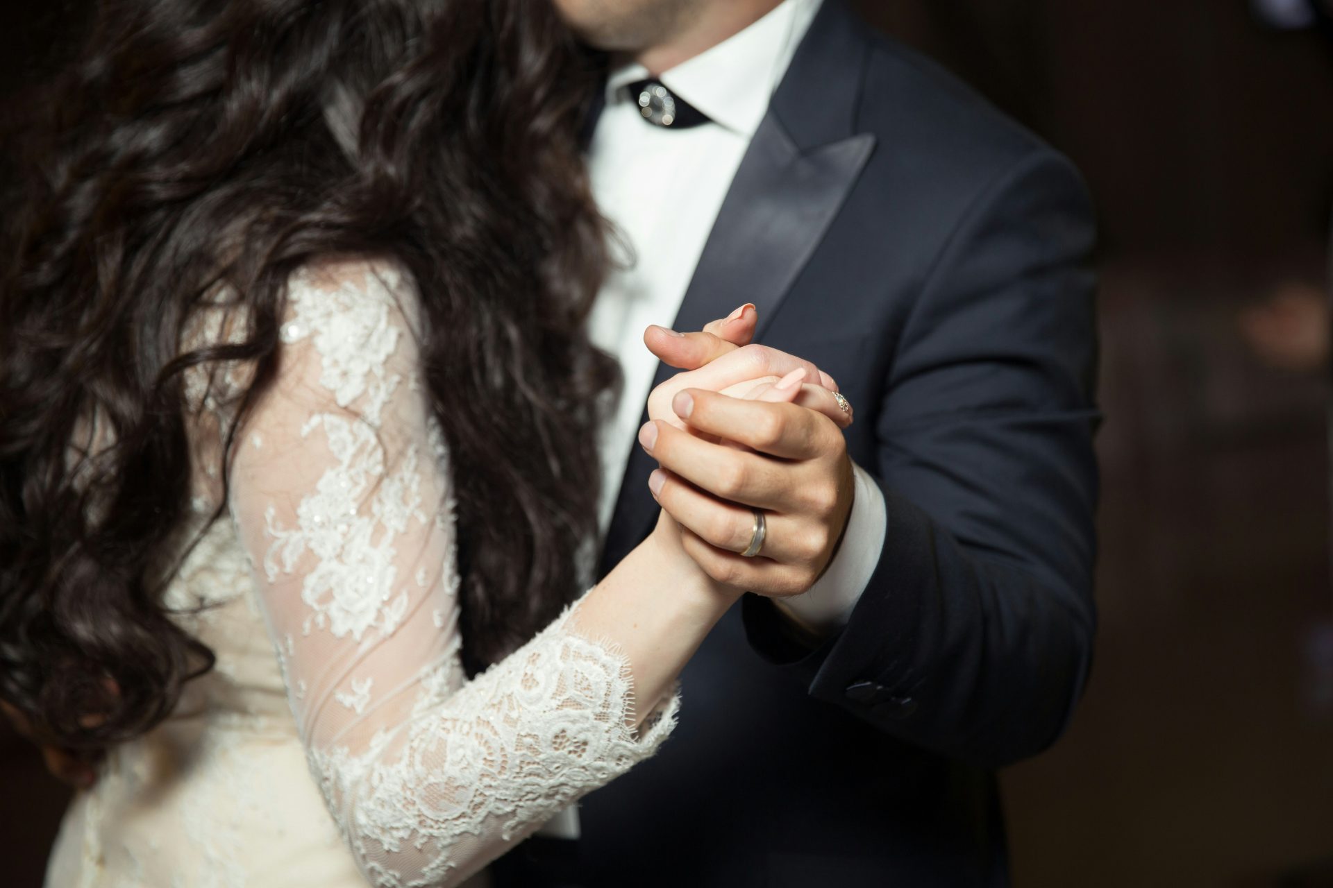 Main des mariés se tenant pour une danse, avec un focus sur leurs alliances.