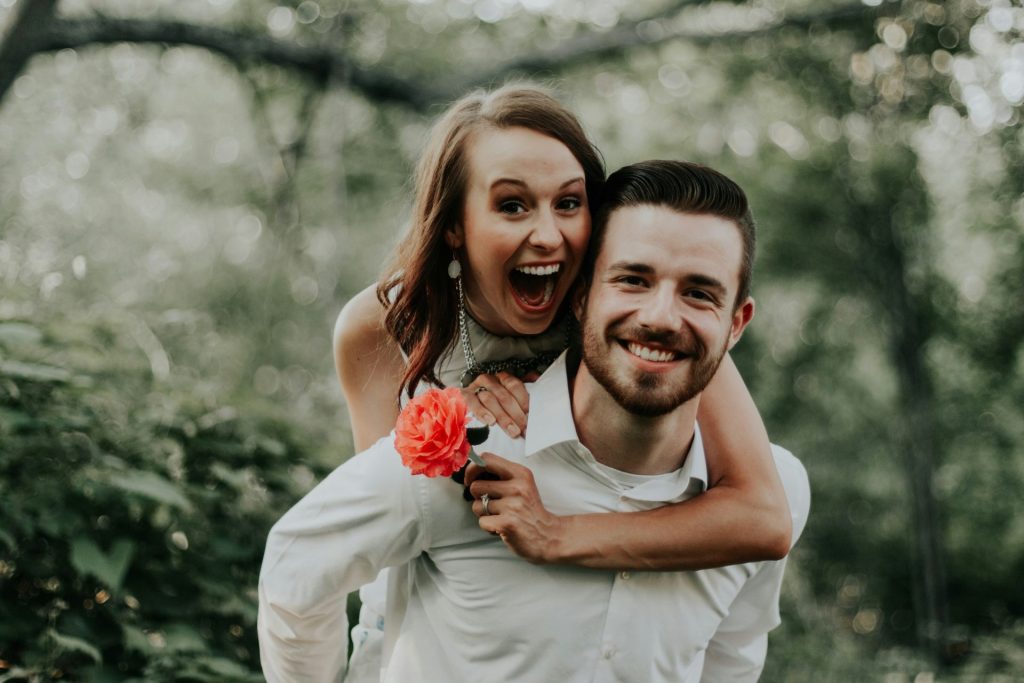 Mariée tenant une rose et marié souriant, tous deux regardant la caméra avec complicité.